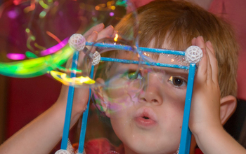 Child blowing bubbles through a 3D geometric shape