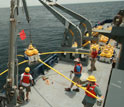 Photo of a crew on a ship using a crane to deploy a receiver in the ocean