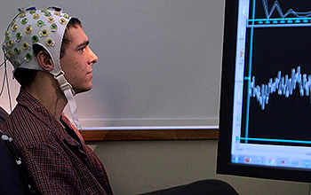 Person wearing EEG cap seated in front of computer screen showing brain activity