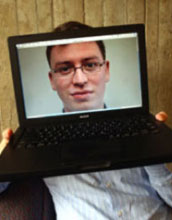 Luis von Ahn holding a laptop blocking his face with an image of his face in the monitor.