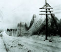Photo of a snow-covered road and telephone wires sagging under a heavy burden of snow.