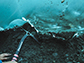 researcher reaches with an ice axe on frozen sediment beneath a glacier